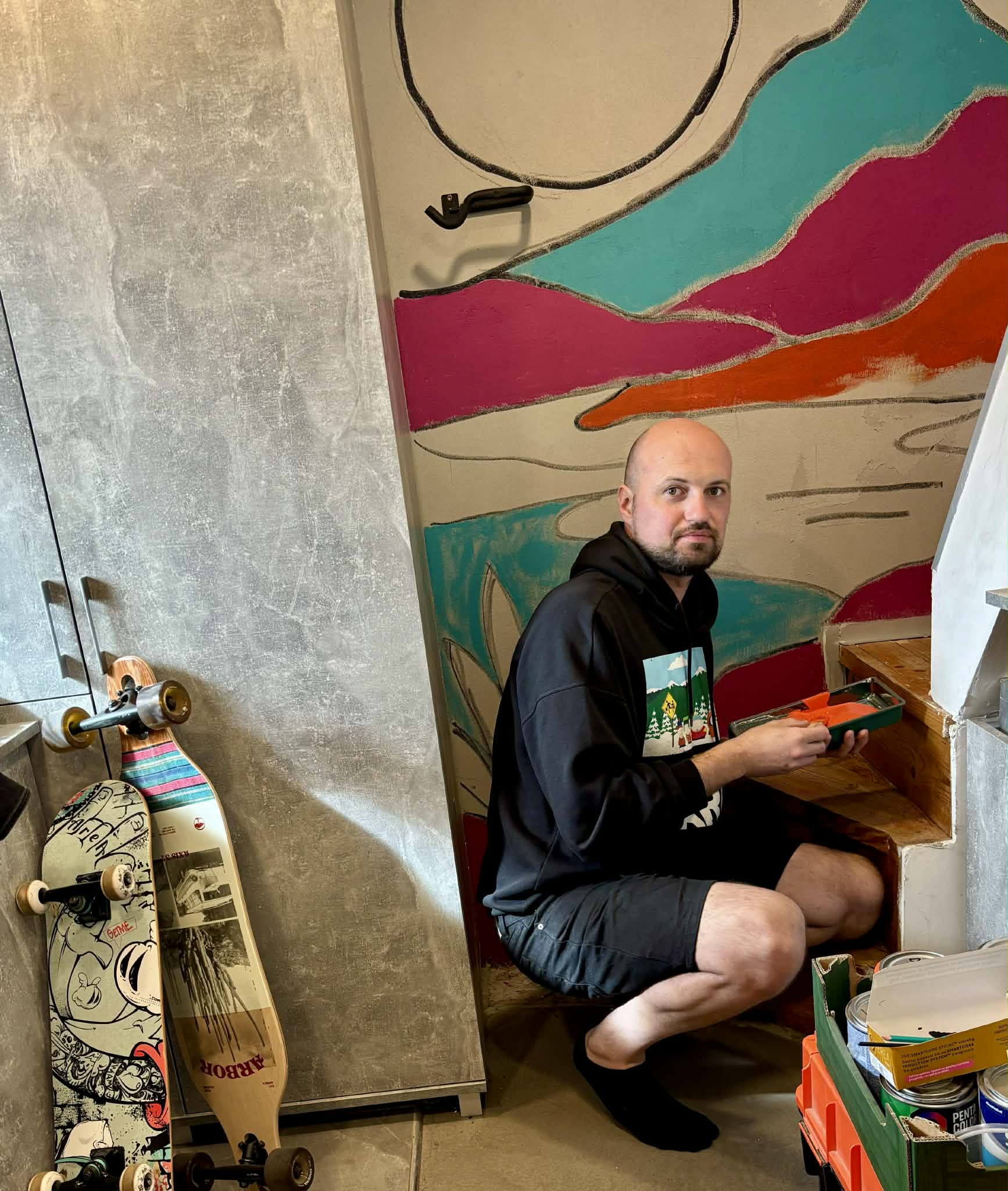 Lukas by a hand-painted wall mural at home, with longboards beside him